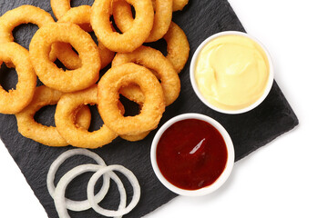 Black board with fried breaded onion rings and different sauces on white background