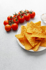 Plate of nacho chips with tomatoes, salt and dip on white background