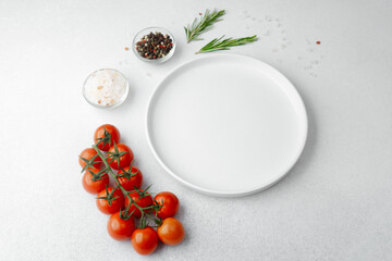 Empty white plate with salt, pepper, tomatoes and rosemary on white background