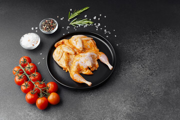 Marinated quail on black plate with tomatoes, herbs and spices on dark background