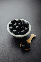 Black olives in white bowl and wooden spoon on dark table