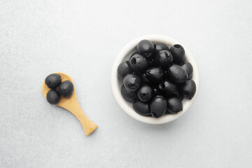 Black olives in white bowl and wooden spoon on bright background