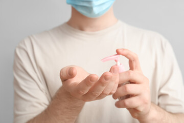 Young man with sanitizer on light background, closeup