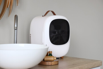 Cosmetic refrigerator with products and sink on chest of drawers in bathroom