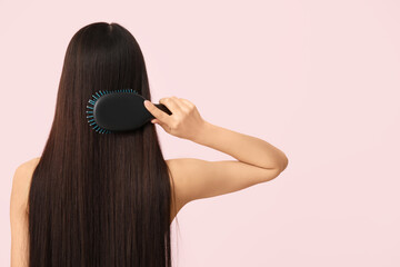 Young woman brushing her long brown straight hair on pink background, back view
