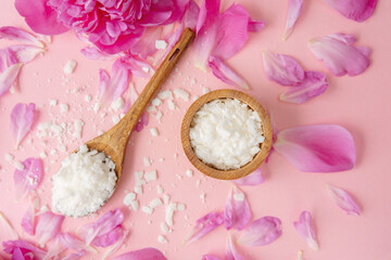 Wooden spoon and bowl with soy wax flakes surrounded by pink petals