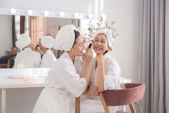 Beauty, skincare, aging, comparison, lifestyle Asian retired mother and daughter in bathrobes sharing bonding moment at vanity table, makeup routine showing generational charm and natural family care - Powered by Adobe