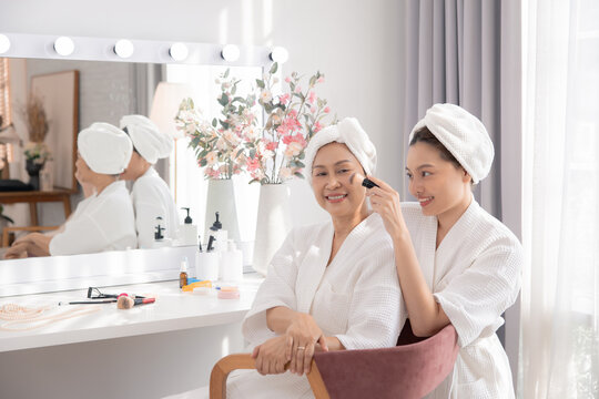 Beauty, skincare, aging, comparison, lifestyle Asian retired mother and daughter in bathrobes sharing bonding moment at vanity table, makeup routine showing generational charm and natural family care