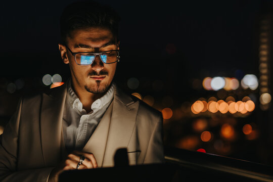 A focused business professional working late at night, illuminated by city lights, as he concentrates on an important project, reflecting determination and dedication in a modern urban environment.