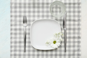 Beautiful table setting with plate,  cutlery, glass, flowers and checkered napkin on white...