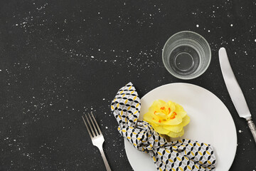 Beautiful table setting with plate, napkin, glass, cutlery and flower on black background