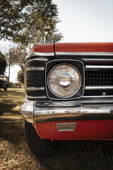 Front view of a red classic car, highlighting the single headlight, metallic frame, and chrome bumper finish.