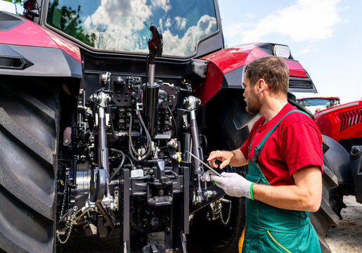 Male mechanic checking farm tractor using digital tablet in rural area - Powered by Adobe