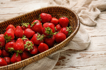 Wicker bowl with sweet fresh strawberries on white wooden background