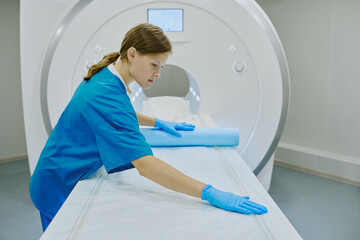 Caucasian young adult woman preparing MRI scanner by spreading protective sheet on examination...