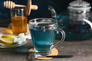 Cup of butterfly pea flower tea and teaspoon on grunge background, closeup