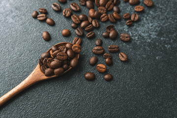 Coffee beans in wooden spoon closeup on dark background