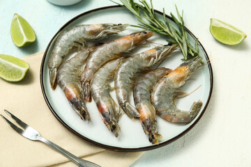 Plate with fresh raw shrimps, rosemary and lime on light blue background