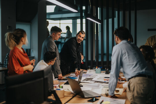A diverse group of business colleagues gather around a table in a modern office, engaged in a lively brainstorming session. They discuss ideas, strategies, and solutions to achieve success together. - Powered by Adobe