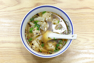 Wonton soup in a porcelain bowl on a wood-grain tabletop
