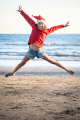 Happy girl jumping on the beach wearing Santa hat