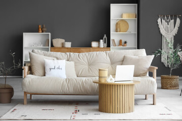 Comfortable sofa and coffee table with laptop in interior of living room
