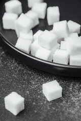 White sugar cubes scattered on a black tray with sugar dust