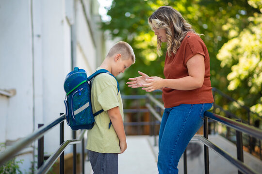 Mother scolding her sad son with backpack after school conflict.  

