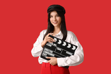Young happy female film director with movie clapper on red background
