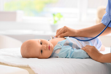 Female pediatrician with stethoscope listening to little baby on couch in clinic, closeup