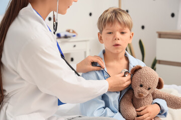 Female doctor listening to little boy ill with chickenpox in bedroom