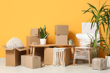 Wooden table, houseplants and cardboard boxes near orange wall. Moving house concept