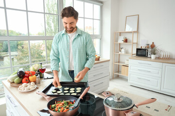 Handsome bearded man putting zucchini slices on baking tray in kitchen