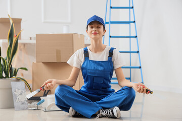 Female decorator with putty knives meditating in room