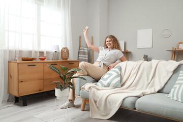 Smiling young woman with air conditioner remote control in living room