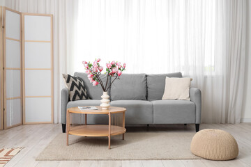 Interior of living room with sofa, folding screen and magnolia flowers in vase