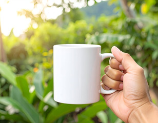 Obraz premium White mug mockup in hand with green nature background, perfect for branding and product design.