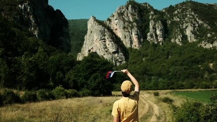 Female traveler in a yellow shirt waves the Serbian flag towards dramatic mountain peaks, celebrating culture and adventure in nature. Rear view. Stara Planina national park, Serbia country - Powered by Adobe