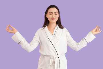 Young woman in pajamas meditating on lilac background