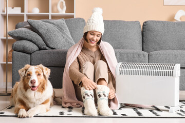 Young woman in winter clothes with blanket and Australian Shepherd dog sitting on floor near heater...