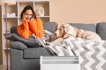 Young woman with blanket and Australian Shepherd dog lying on sofa near heater at home