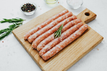 Raw pork sausages on wooden board with spices and rosemary