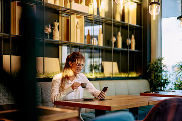 Woman Enjoying Coffee While Checking Her Smartphone in a Cafe