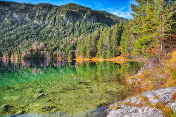 Stunning autumn landscape of Eibsee Lake in front of Zugspitze summit under sunlight.