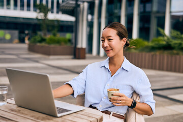 Asian Business Woman Working Outdoors with Coffee and Laptop at Urban Setting