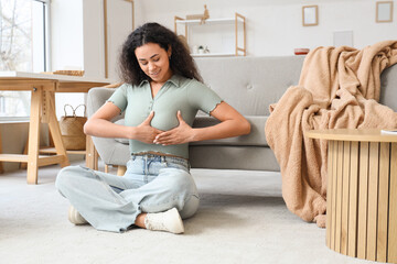 Young African-American woman checking her breast on floor at home. Cancer awareness concept