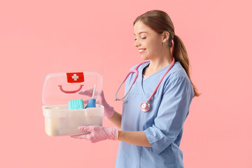 Young female doctor with first aid kit on pink background