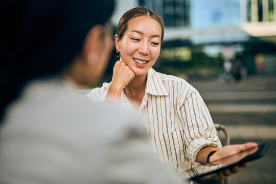 Asian Businesswoman Collaborating Outdoor With a Colleague in Modern Urban Setting - Powered by Adobe