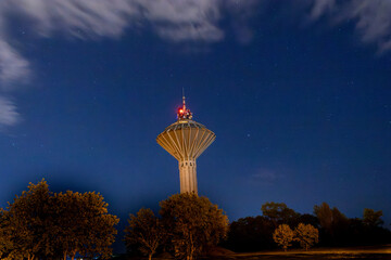 Night view of a water tower glowing under a clear starry sky with clouds, symbolizing...