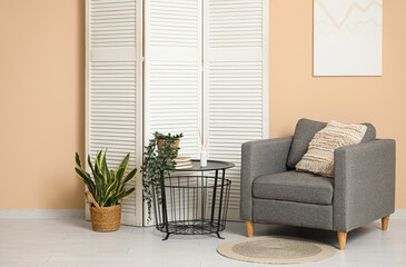 Interior of living room with folding screen, armchair and table near beige wall